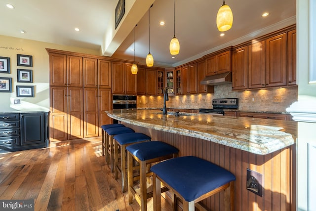 kitchen featuring brown cabinets, hardwood / wood-style flooring, a sink, under cabinet range hood, and stainless steel electric range oven