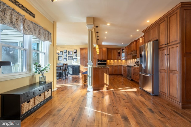 kitchen with brown cabinets, stainless steel appliances, hardwood / wood-style flooring, a kitchen breakfast bar, and tasteful backsplash