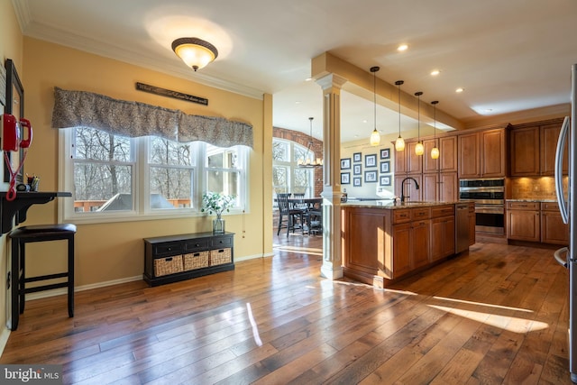 kitchen with light stone countertops, ornamental molding, decorative columns, brown cabinetry, and dark wood-style flooring