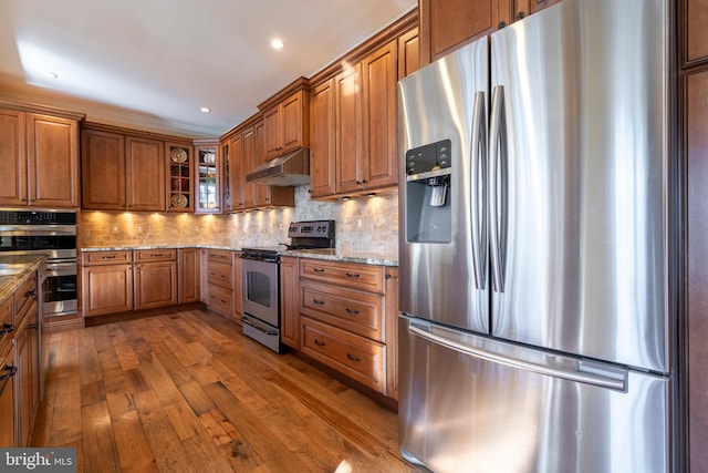 kitchen with light stone counters, brown cabinetry, under cabinet range hood, and stainless steel appliances