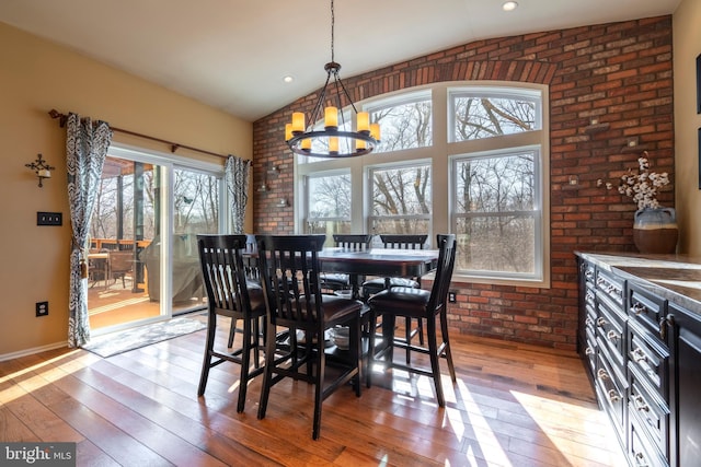 dining space featuring an inviting chandelier, brick wall, light wood-style floors, and vaulted ceiling