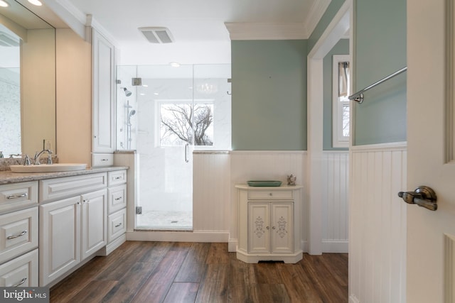 bathroom with ornamental molding, wood finished floors, wainscoting, a shower stall, and vanity