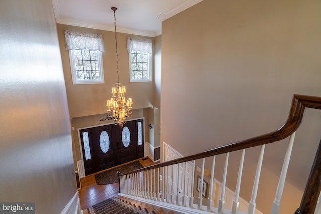 foyer with stairs, ornamental molding, a high ceiling, wood finished floors, and a notable chandelier