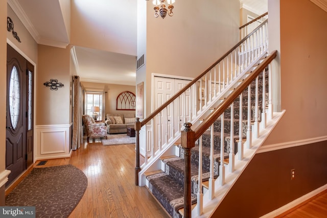 entrance foyer featuring hardwood / wood-style floors, crown molding, visible vents, and wainscoting