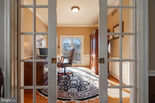 office area with a decorative wall, wainscoting, french doors, and crown molding