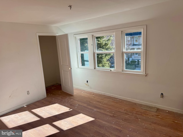 empty room featuring lofted ceiling, wood finished floors, and baseboards