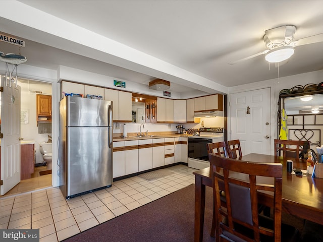 kitchen with under cabinet range hood, light tile patterned floors, freestanding refrigerator, electric stove, and a sink