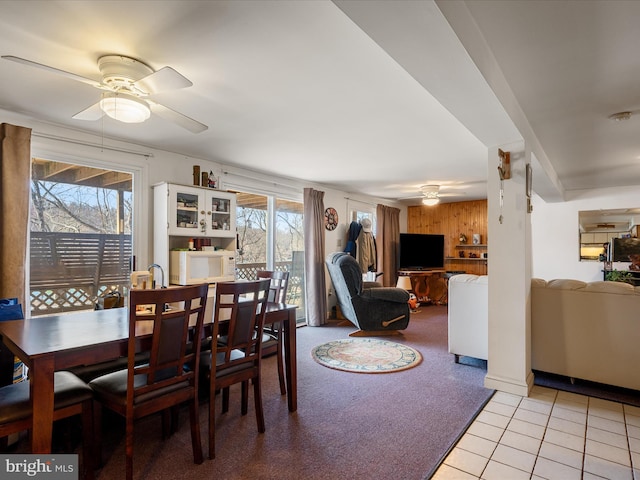 dining area with light tile patterned floors, light carpet, wooden walls, and ceiling fan