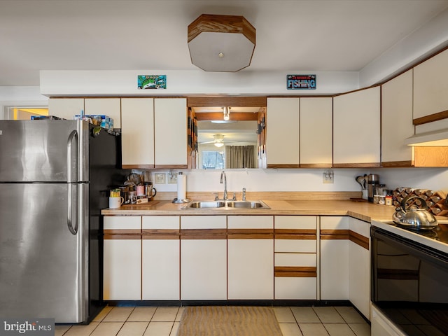 kitchen featuring light countertops, electric range oven, light tile patterned floors, freestanding refrigerator, and a sink