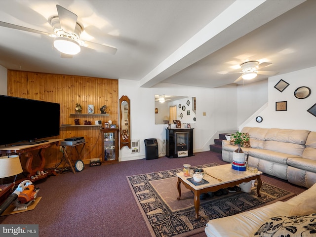 carpeted living room with arched walkways, wood walls, stairs, and a ceiling fan