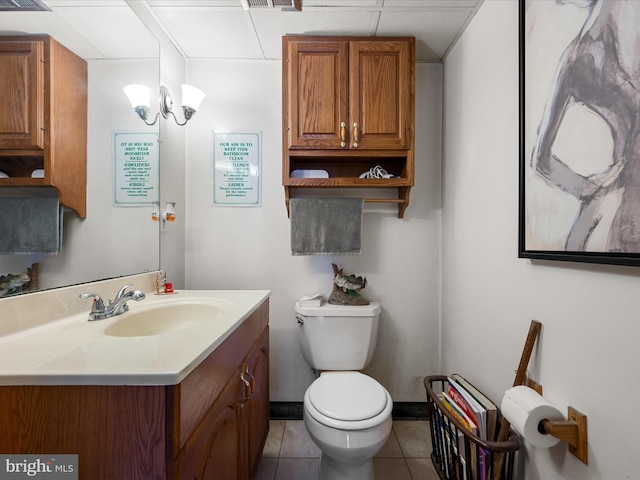 half bath featuring tile patterned flooring, a drop ceiling, toilet, a notable chandelier, and vanity