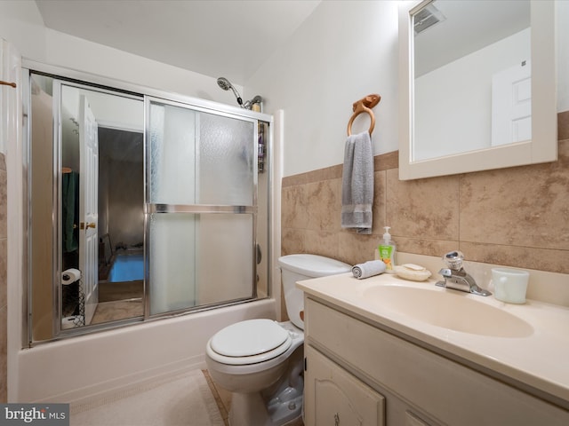 bathroom featuring vanity, visible vents, tile walls, toilet, and combined bath / shower with glass door