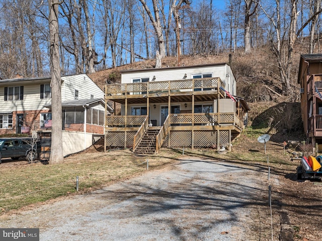 view of front facade with a front lawn, a deck, stairs, and a sunroom