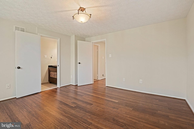 unfurnished bedroom featuring baseboards, visible vents, ensuite bath, wood finished floors, and a textured ceiling