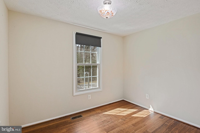 spare room featuring hardwood / wood-style flooring, baseboards, visible vents, and a textured ceiling