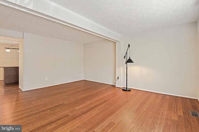 unfurnished room with wood-type flooring, visible vents, a textured ceiling, and baseboards