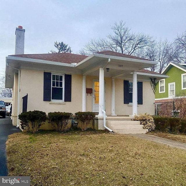 view of front of home with a shingled roof, a porch, a chimney, and stucco siding