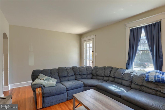 living area featuring arched walkways, a healthy amount of sunlight, and wood finished floors