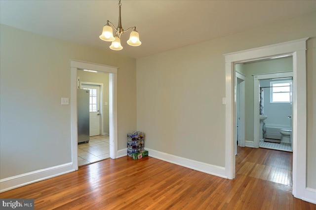 unfurnished room with a notable chandelier, baseboards, and wood-type flooring