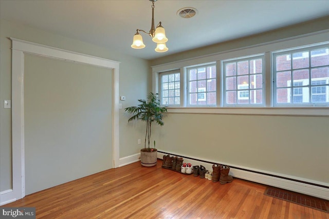 unfurnished room with visible vents, a baseboard heating unit, an inviting chandelier, and wood finished floors