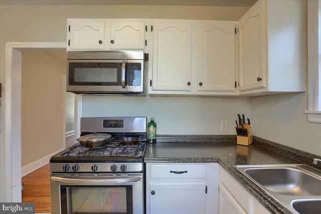 kitchen with white cabinetry, dark countertops, appliances with stainless steel finishes, and a sink