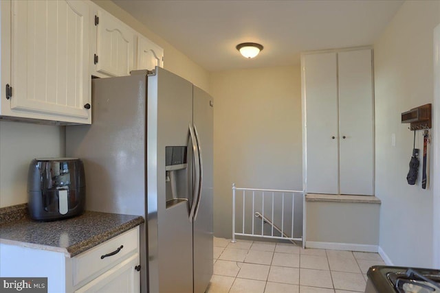 kitchen featuring light tile patterned floors, stainless steel fridge, white cabinets, and baseboards