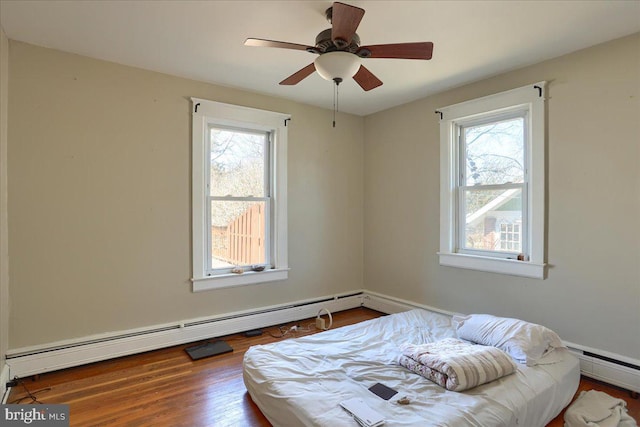 bedroom with a baseboard heating unit, multiple windows, and wood finished floors