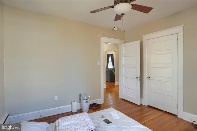 bedroom featuring a ceiling fan, wood finished floors, baseboards, and baseboard heating