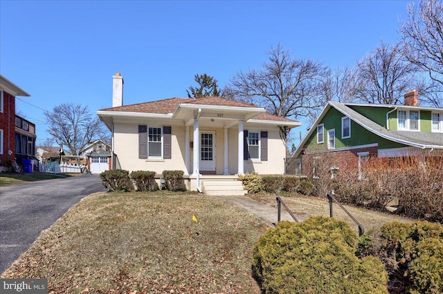 bungalow with stucco siding, roof with shingles, a porch, and a chimney