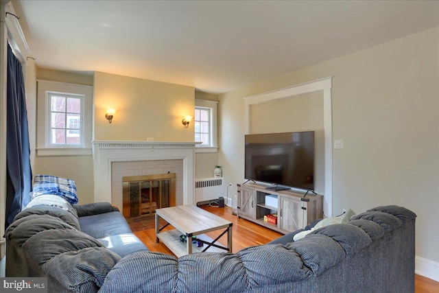 living area featuring a brick fireplace, radiator heating unit, baseboards, and wood finished floors