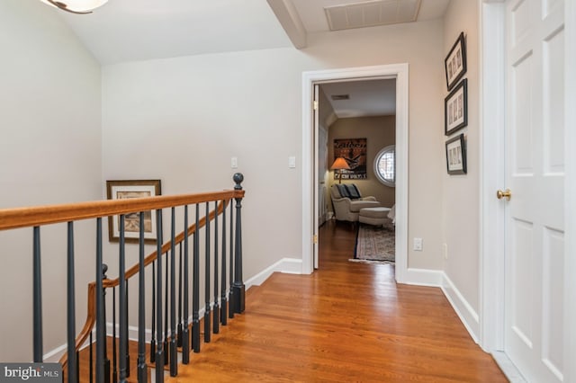 hall with baseboards, visible vents, wood finished floors, and an upstairs landing