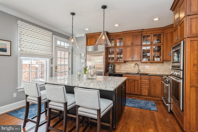 kitchen featuring a breakfast bar area, brown cabinetry, crown molding, and built in appliances