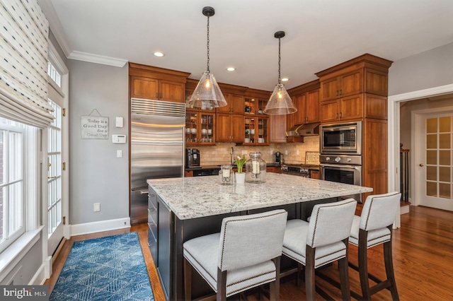 kitchen featuring brown cabinets, dark wood-style flooring, built in appliances, extractor fan, and backsplash