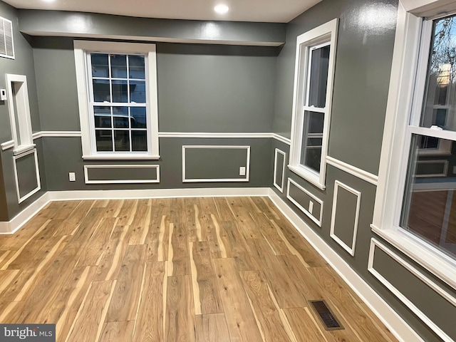 spare room featuring wood finished floors, visible vents, and a decorative wall