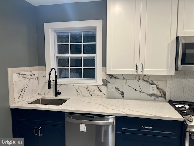 kitchen with white cabinets, a sink, light stone countertops, stainless steel appliances, and backsplash