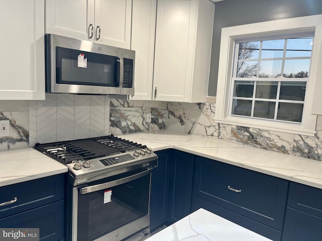 kitchen featuring stainless steel appliances, blue cabinetry, backsplash, and white cabinets