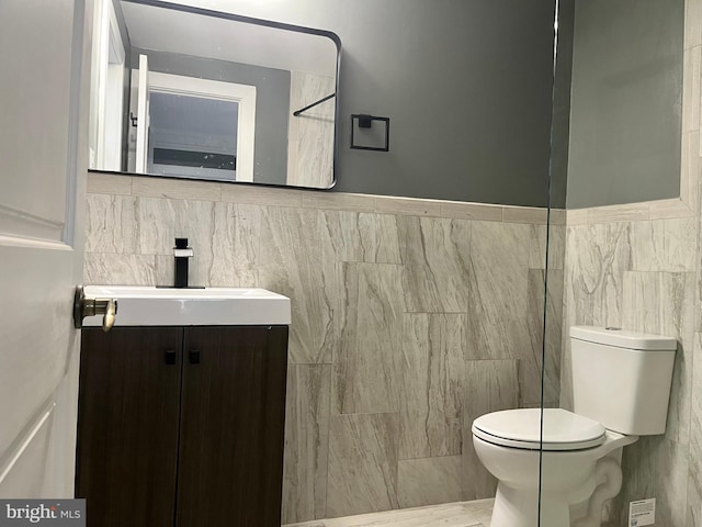 bathroom featuring toilet, vanity, and tile walls