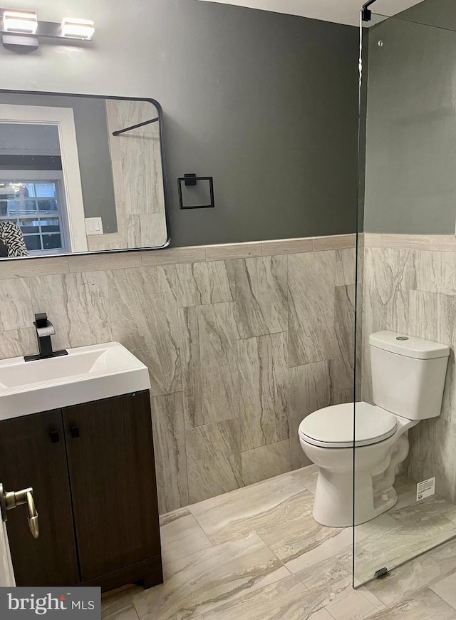 bathroom featuring toilet, wainscoting, tile walls, and vanity