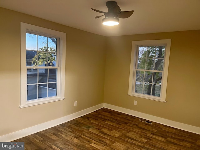 spare room with dark wood-type flooring, a ceiling fan, visible vents, and baseboards