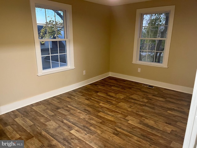 unfurnished room featuring dark wood-style floors, visible vents, and baseboards