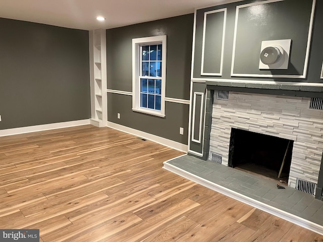 unfurnished living room featuring recessed lighting, a fireplace with raised hearth, baseboards, and wood finished floors