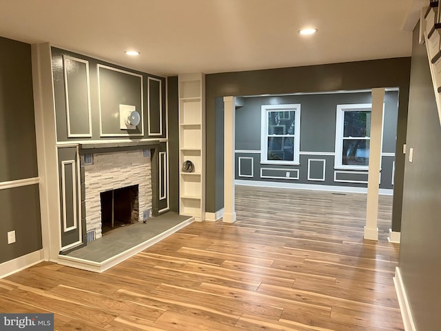 unfurnished living room with baseboards, a stone fireplace, light wood-style flooring, and recessed lighting