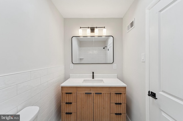 bathroom with vanity, visible vents, walk in shower, tile walls, and toilet