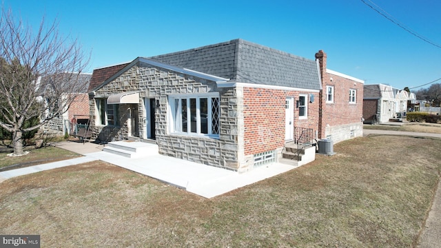 exterior space featuring mansard roof, a shingled roof, a front lawn, stone siding, and brick siding