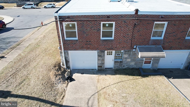 rear view of house with a garage, stone siding, brick siding, and driveway