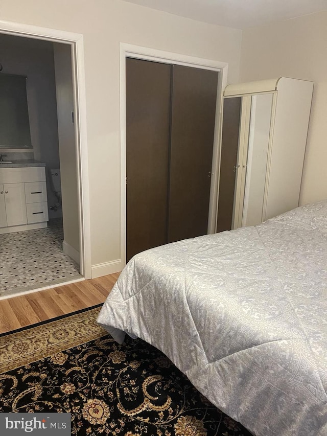 bedroom with light wood-type flooring, baseboards, and connected bathroom