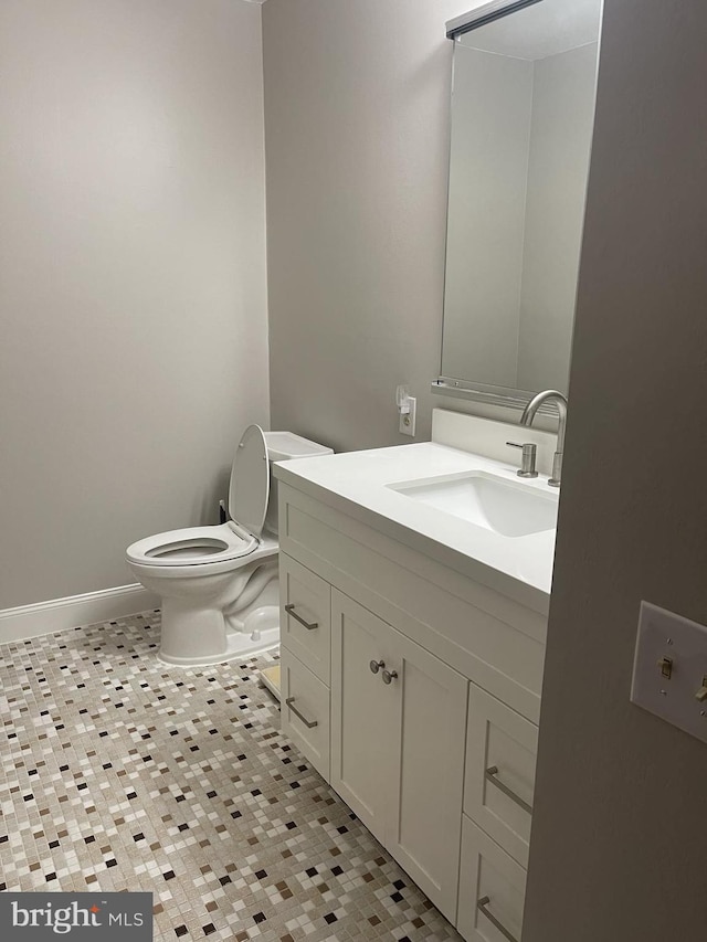 half bathroom featuring toilet, baseboards, and vanity