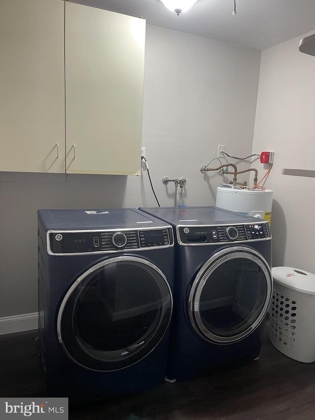 clothes washing area featuring washing machine and dryer, water heater, cabinet space, and wood finished floors