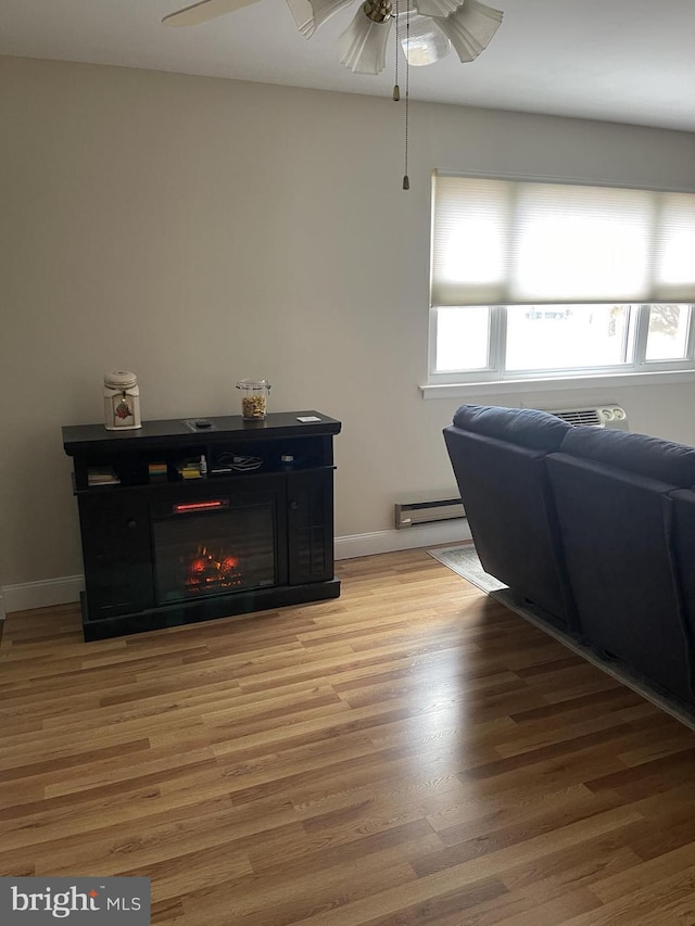 living area with a warm lit fireplace, ceiling fan, a baseboard heating unit, baseboards, and light wood-type flooring