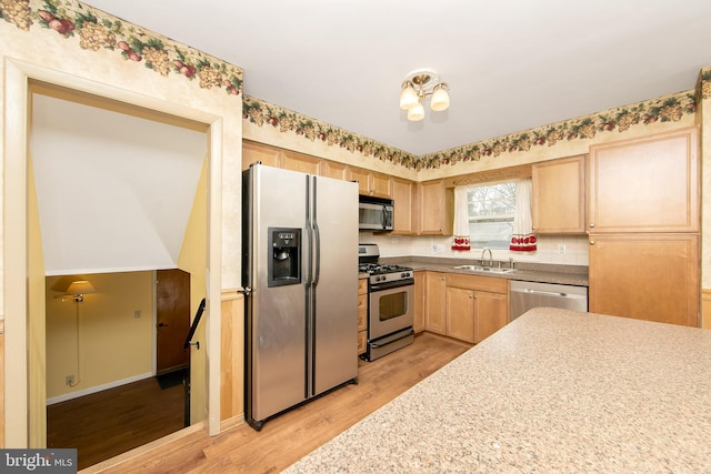 kitchen featuring light wood finished floors, appliances with stainless steel finishes, an inviting chandelier, light brown cabinets, and a sink